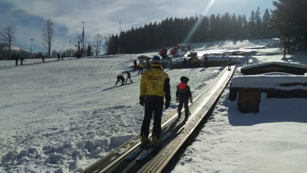 Instruktor i dziecko na nartach wjeżdżają taśmą wyciągową dla początkujących na stoku Karpatka