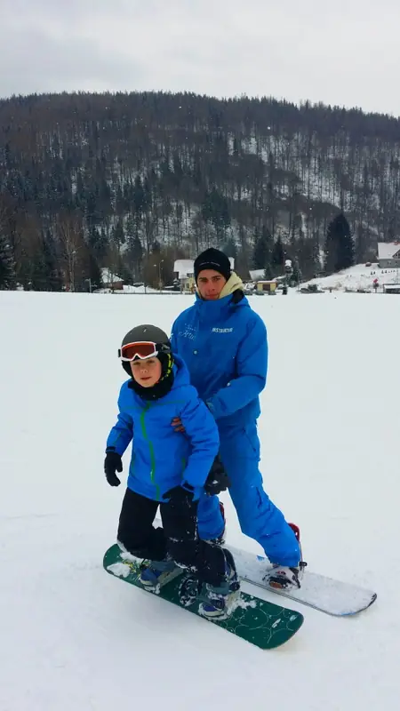 Nauka jazdy na snowboardzie — instruktor z dzieckiem na desce na stoku Karpatka